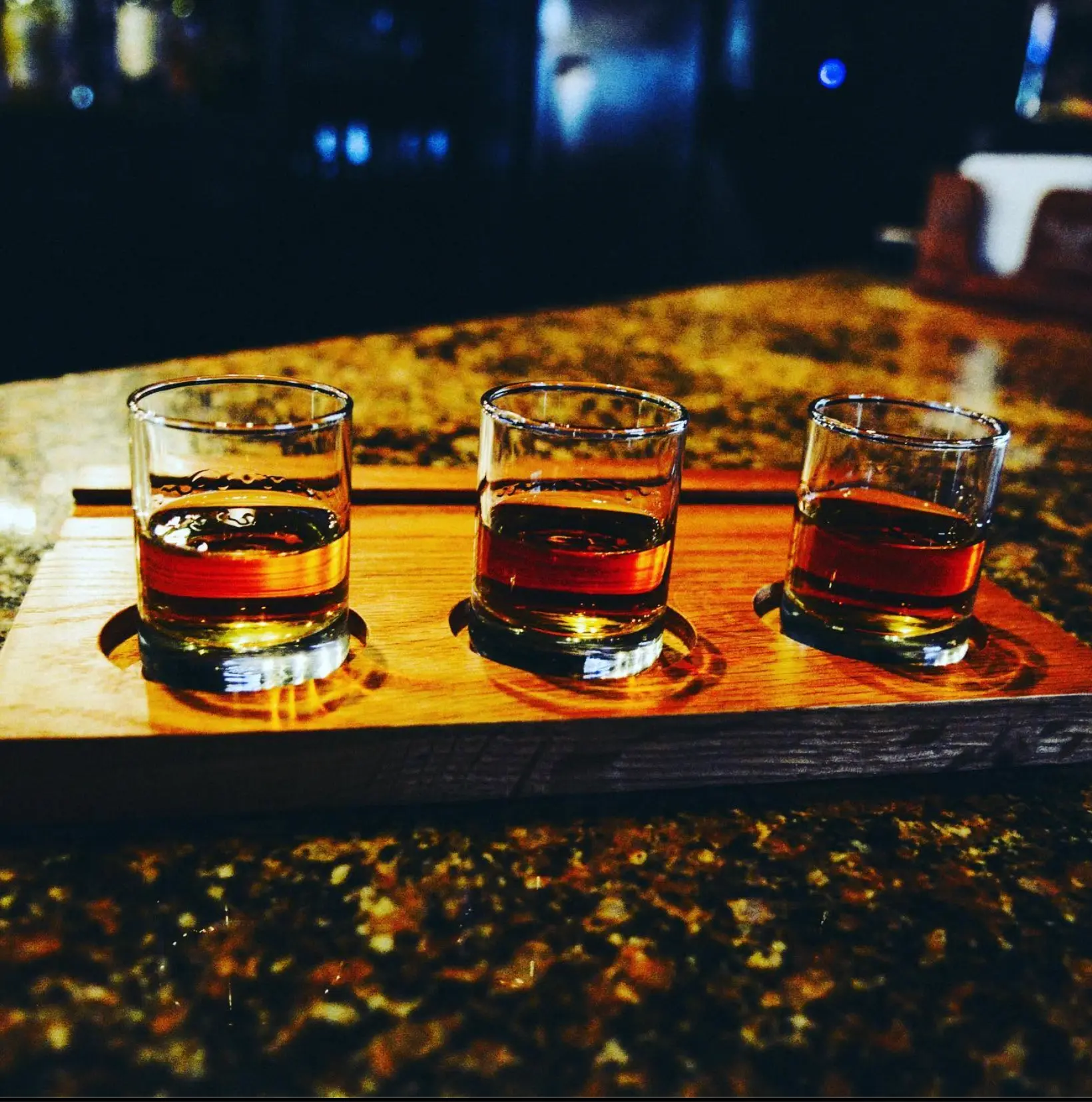 A whiskey flight of three pours on a wooden board