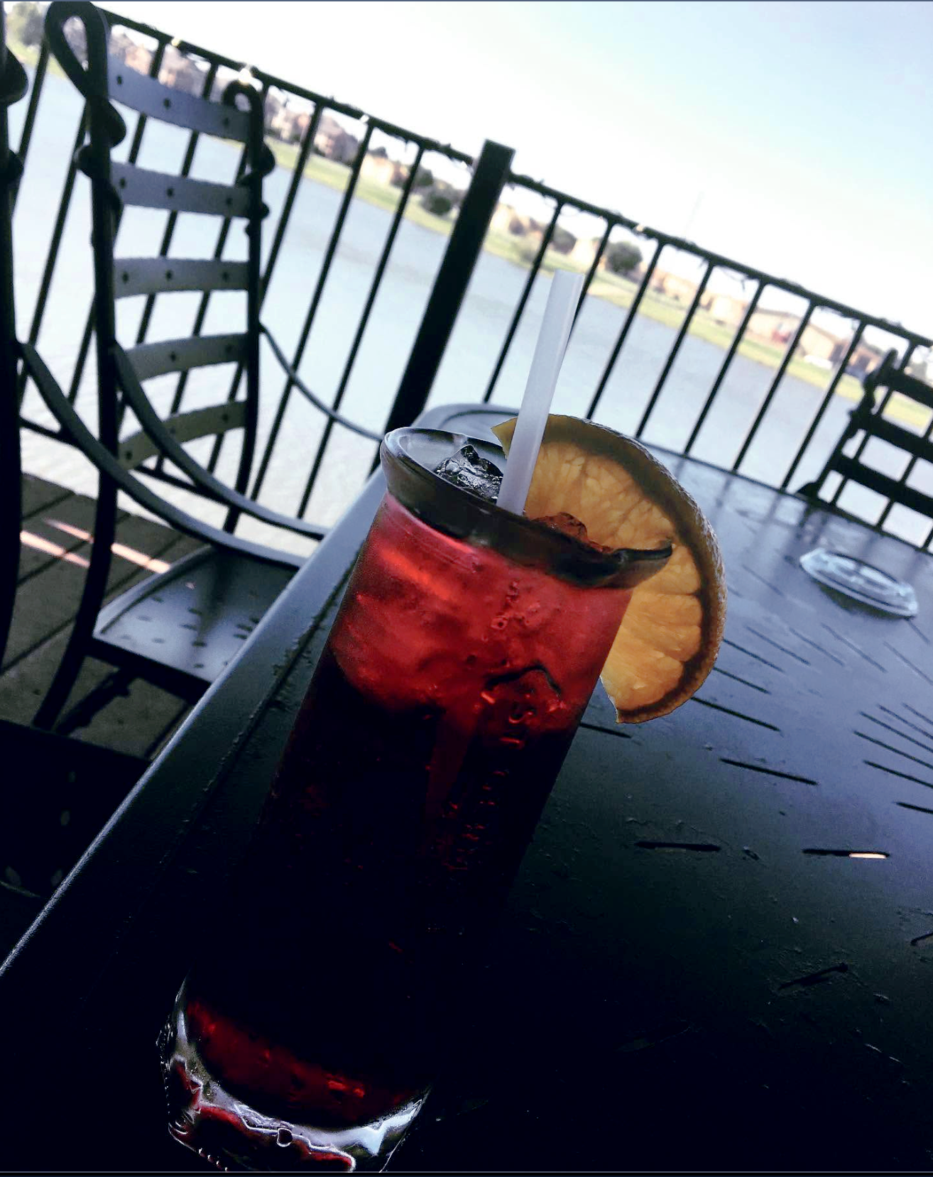 A deep red cocktail with a lemon wheel on The Gas Light's deck, the playa lake beyond the rail