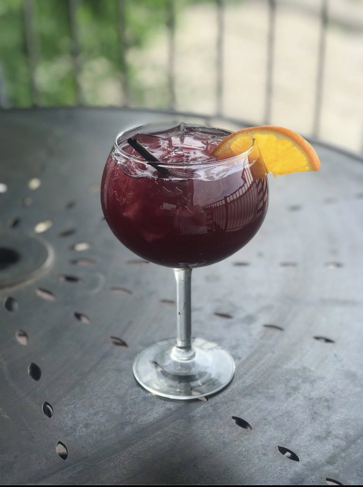 A red cocktail garnished with an orange slice on the outdoor deck