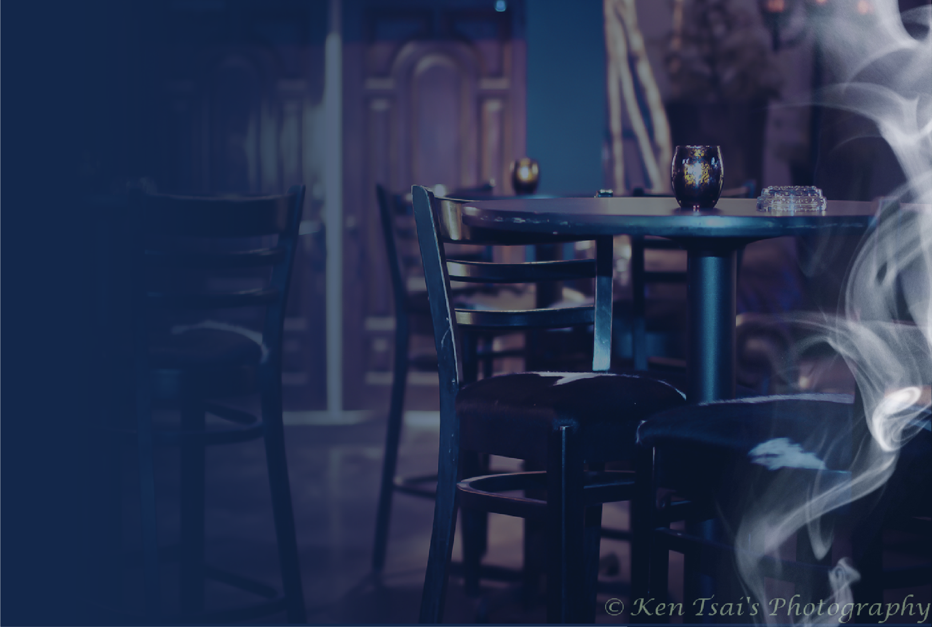 Inside The Gas Light lounge, high tables and bar stools in cool blue light with drifting smoke